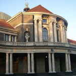 Large, pillared, grey building with a crimson roof.