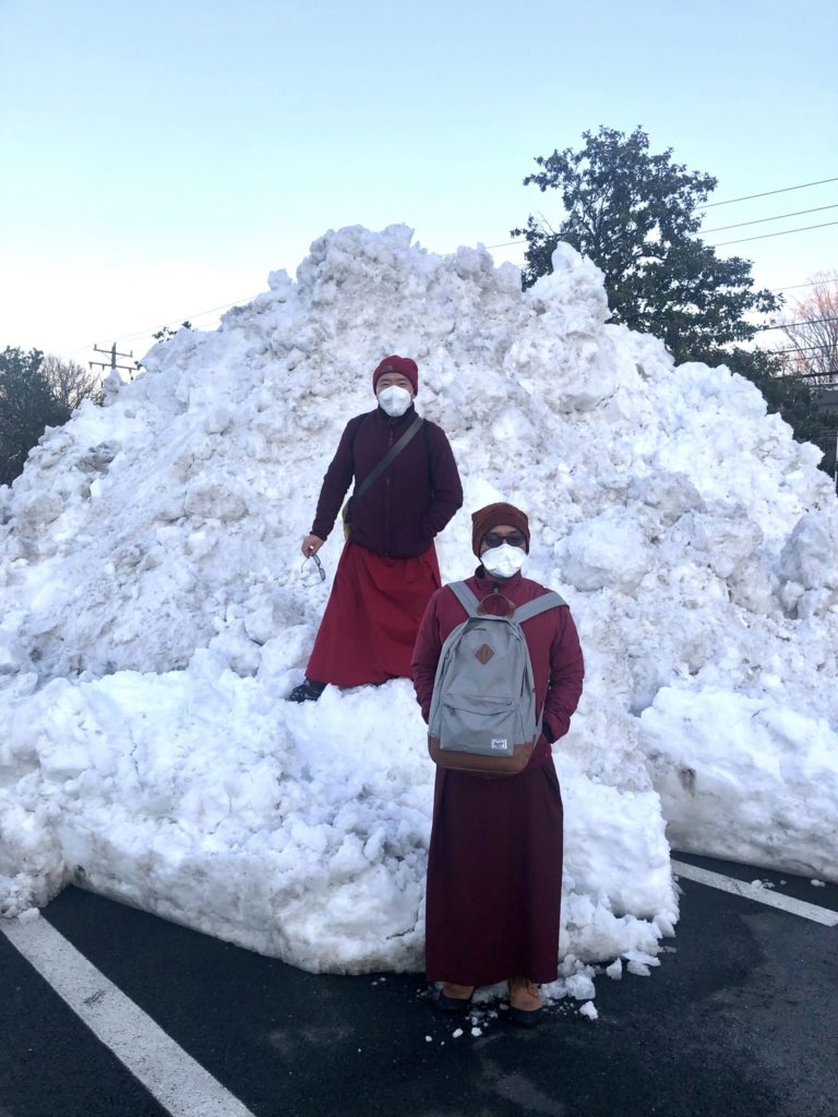 Standing in the middle atop a mound of snow are two men wearing red robes and hats.