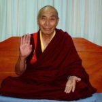 Khenpo Kunga Wanchuk sits in a crossed leg position with his hands in the abhaya mudra of fearlessness and peace.