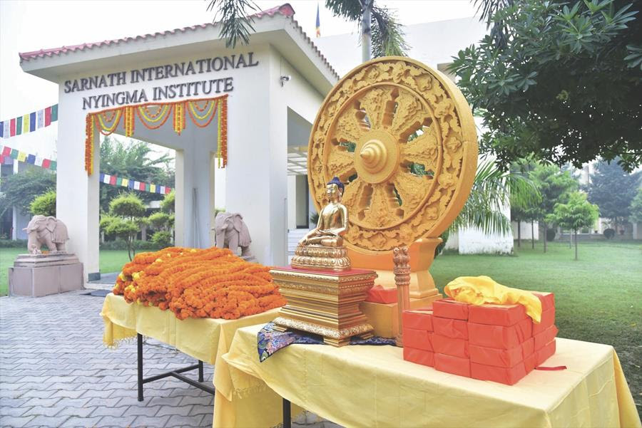 Dharma wheel with a golden Buddha statue in front of it. White gate with 