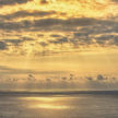 A gorgeous sunset begins over the ocean with clouds in the distance