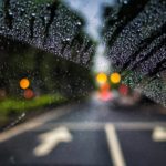 Looking through a car window at the road ahead. Rain is on the windshield but has been partially cleared away by the windshield wiper.