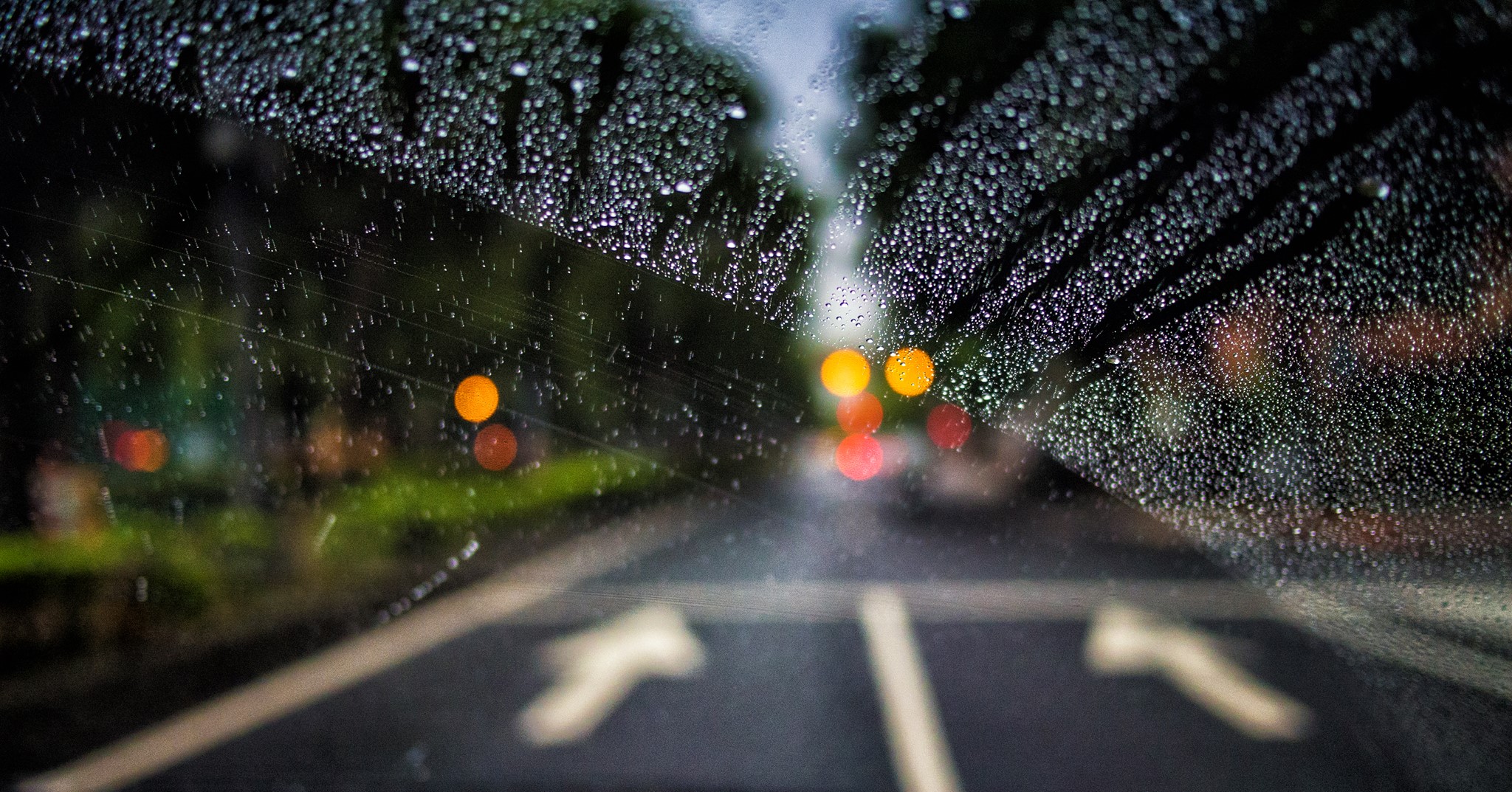 Looking through a car window at the road ahead. Rain is on the windshield but has been partially cleared away by the windshield wiper.
